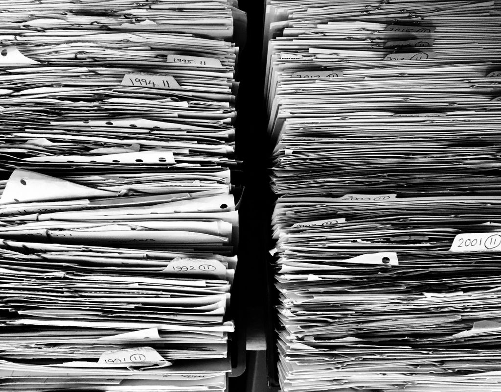 Deux piles de dossiers papier archivés, classés par année, remplissant une étagère