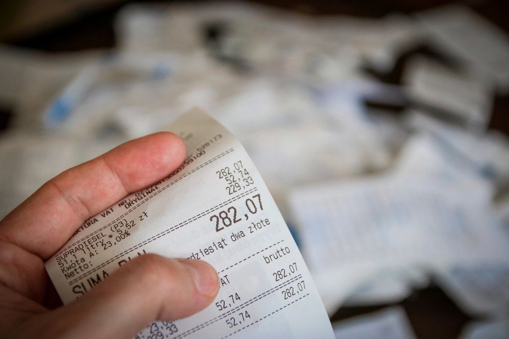 Une main tient un ticket de caisse au-dessus d'une pile de reçus et de factures en papier