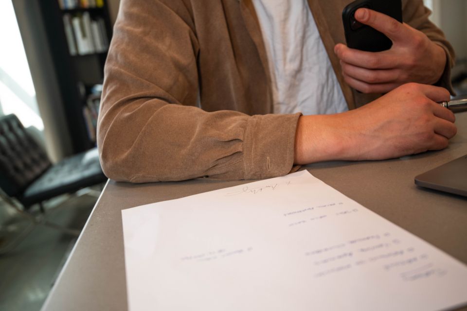 Une personne assise à un bureau clair, un document signé posé devant elle et un téléphone à la main