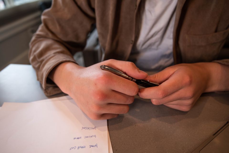 Les mains d'une personne tenant un stylo au-dessus d'un carnet de notes posé sur un bureau
