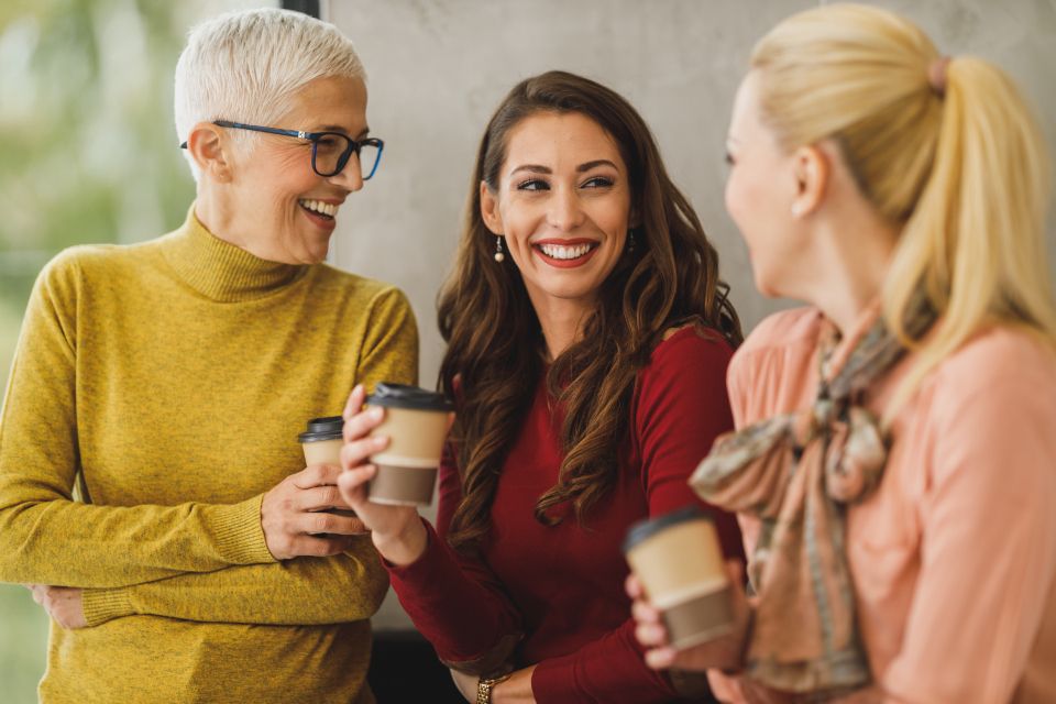 Trois femmes discutent en souriant, un gobelet de café à la main