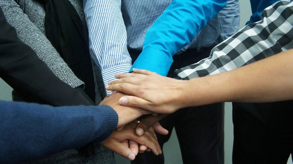 Plusieurs mains posées les unes sur les autres au centre d'un groupe, symbole d'un travail collectif