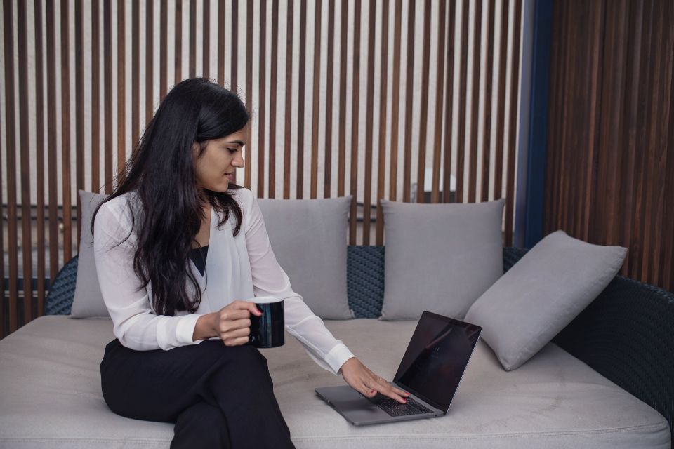 Une personne rédige un message de suivi sur son ordinateur portable, une tasse à la main