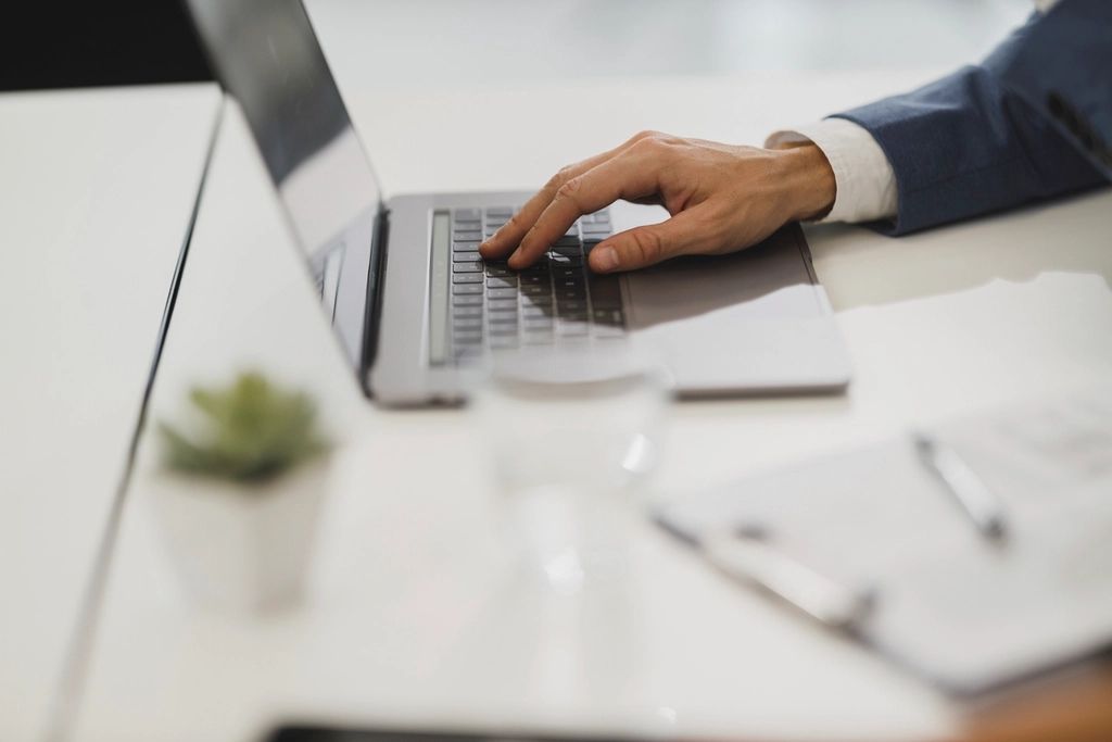 Une main sur le clavier d'un ordinateur portable posé sur un bureau clair et rangé